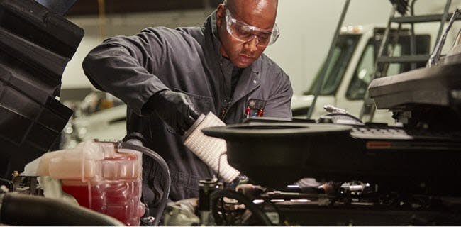 A person wearing safety glasses and gloves working on a car