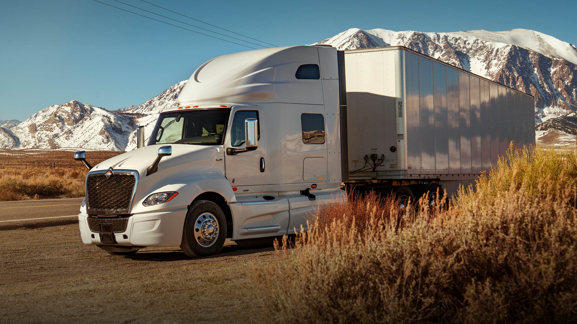 White truck driving along a road with snowy mountains in background